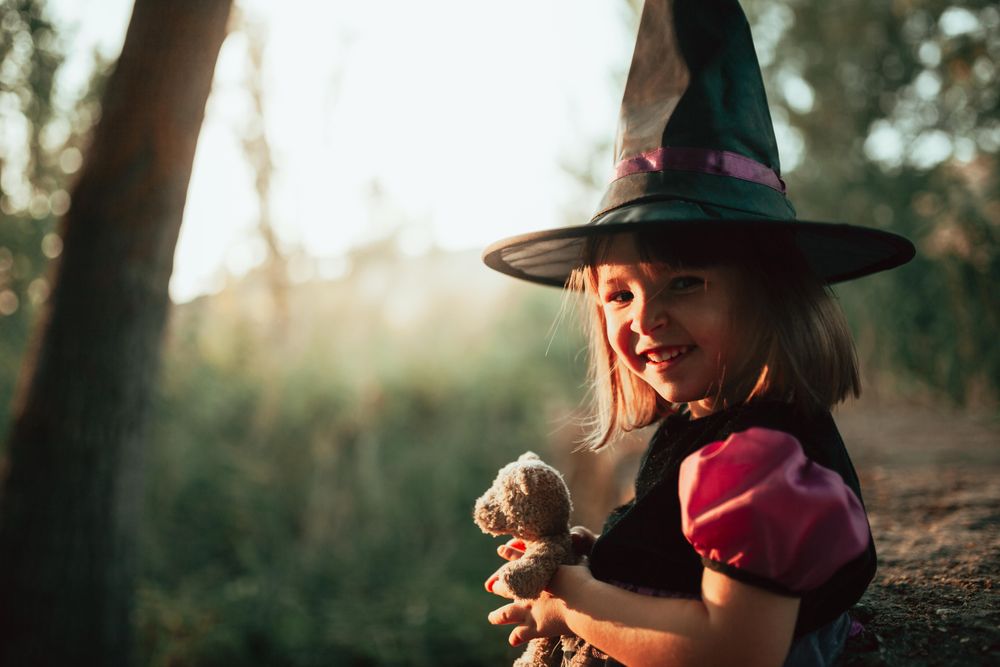 Girl in witch hat with teddy bear in the forest