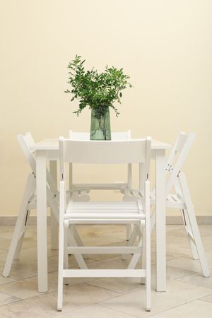 Wooden table with vase with plant and folding chairs against light beige wall