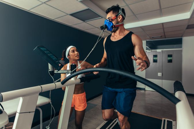 Woman fitness coach giving instruction to male runner on treadmill in laboratory