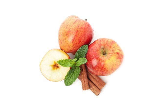 Top view of two apples, leaves, cinnamon sticks, and a pot of honey