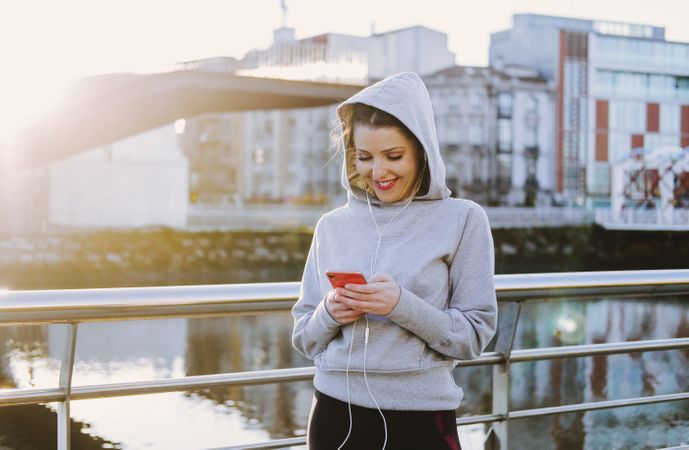 Woman with earphones wearing a hoodie on a embankment