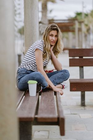 Confident woman with disposable cup of coffee sitting on street bench