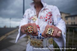 Elvis impersonator showing off flashy rings on sidewalk with blurry, cloudy background 5qkdjb