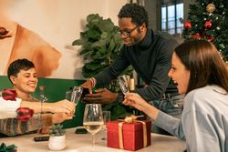 Happy diverse friends sharing and pouring champagne at a festive Christmas party.