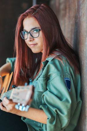 Romantic woman playing guitar leaning on wall