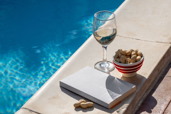 Relaxing by the pool with a book, wine, and a snack on a sunny summer day