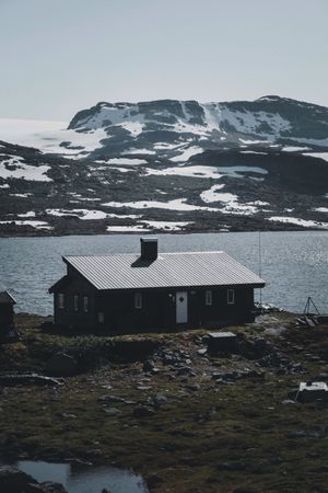 Brown wooden house near snow covered mountain and lake