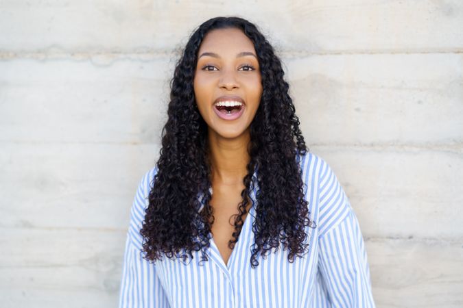 A Joyful Young Woman with Curly Hair Smiling Cheerfully Against a Neutral Background