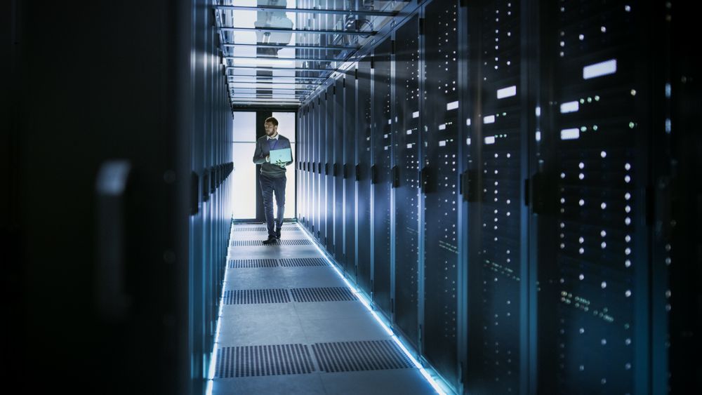 IT Technician Works on Laptop in Big Data Center full of Rack Servers.