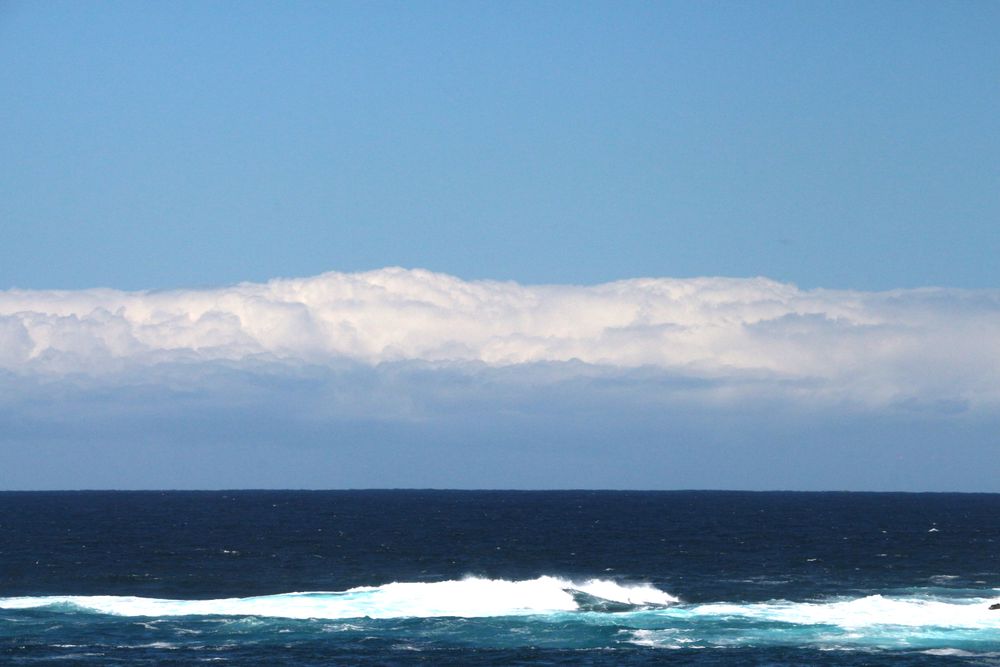 Ocean waves rolling gently under a bright blue sky with clouds in the distance
