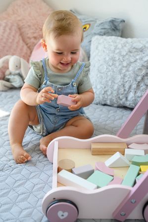 Baby girl playing with toy blocks and cart in bedroom