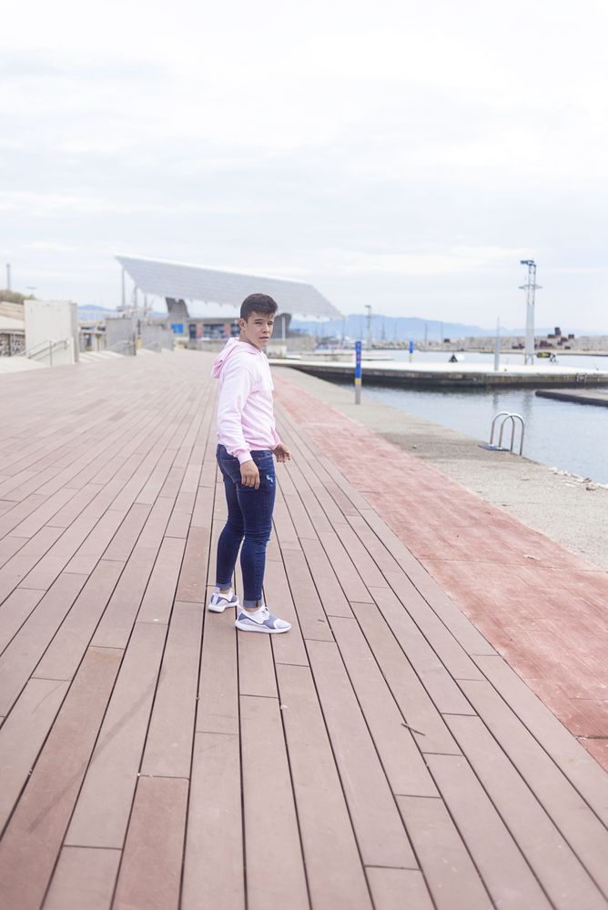 Young male teenager walking along rocky breakwater and looking back at camera