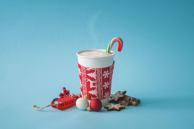 To-go cup of coffee with Christmas sleeve and candy cane, decorations and cookies