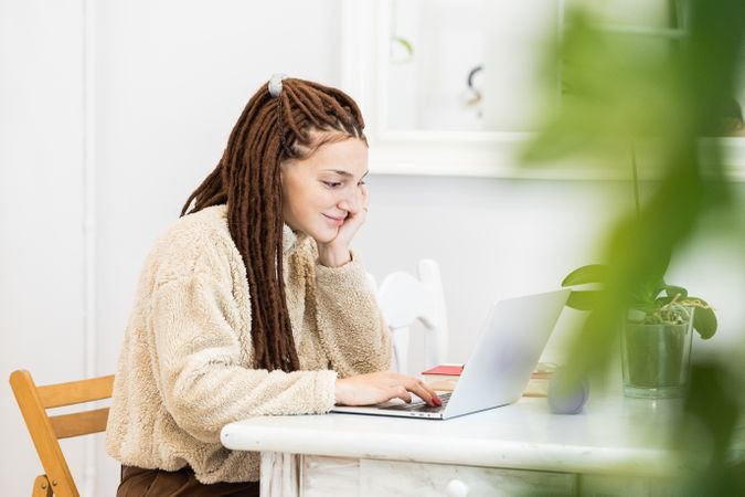 Thoughtful woman with dreadlocks working with a laptop at home