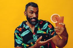 Black male sitting down amazed at his cocktail in yellow room, copy space
