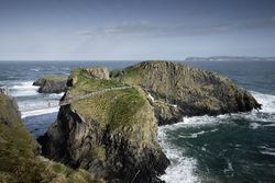 Tourist walking on rope bridge suspended between cliffs in Northern Ireland