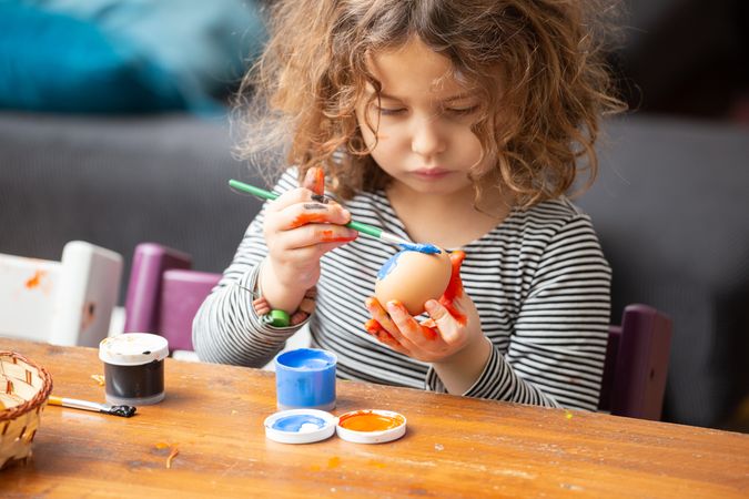 Toddler girl painting egg at table