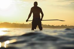 Man with paddle on surf board between waving water at sunset