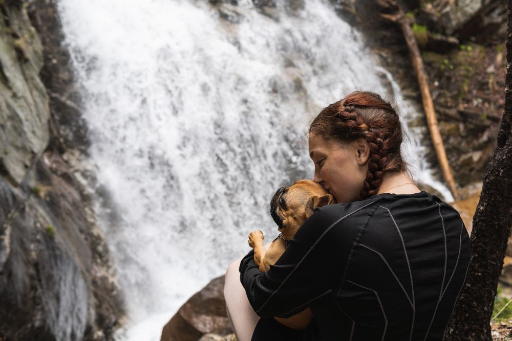 Cheerful traveling woman with dog near waterfall in forest