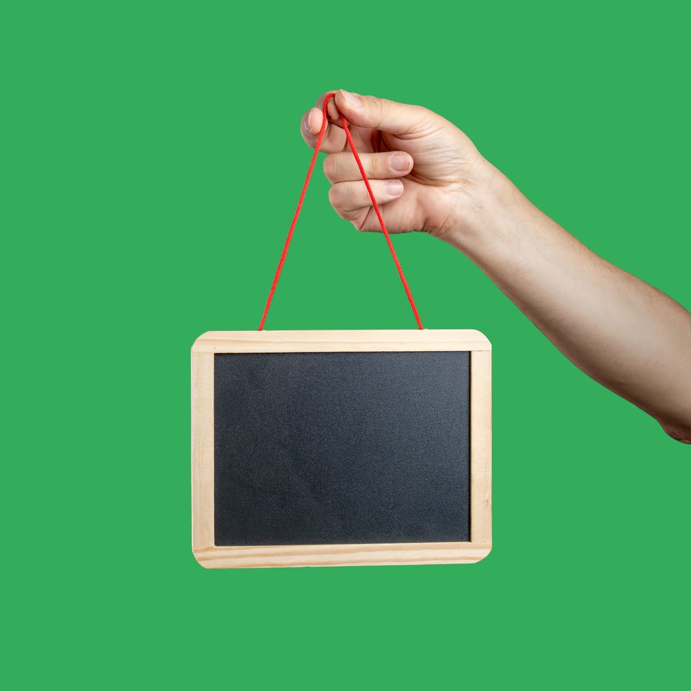 Hand holding a blank chalkboard mockup on a green background.