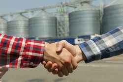 Businessmen shake hands against silos. Agriculture business