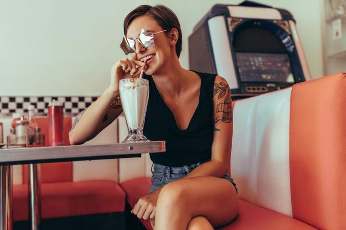 Smiling woman drinking milkshake with a straw sitting at a restaurant table
