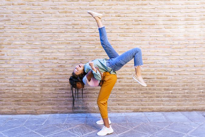 Two close female friends with one lifting the other up in front of brick wall outside