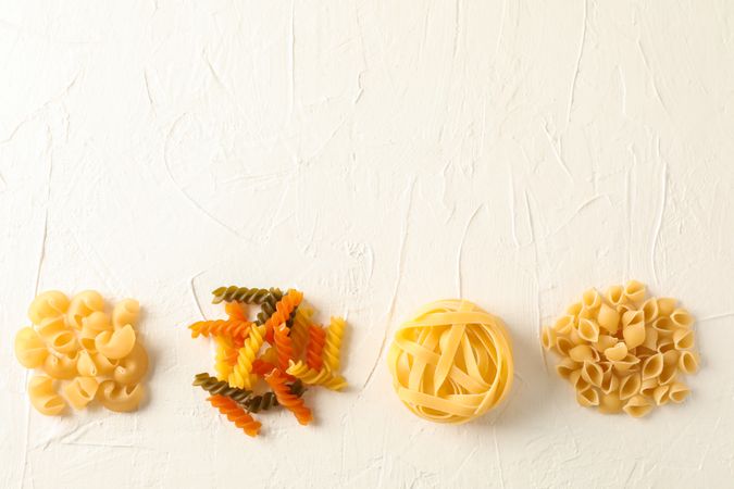 Flat lay composition with different pasta on light background, space for text. Dry uncooked whole pasta