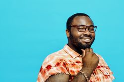 Portrait of a happy man in orange shirt smiling and thinking with hand on chin at camera