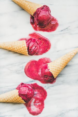 Four cones of dark berry ice cream melting on marble slab