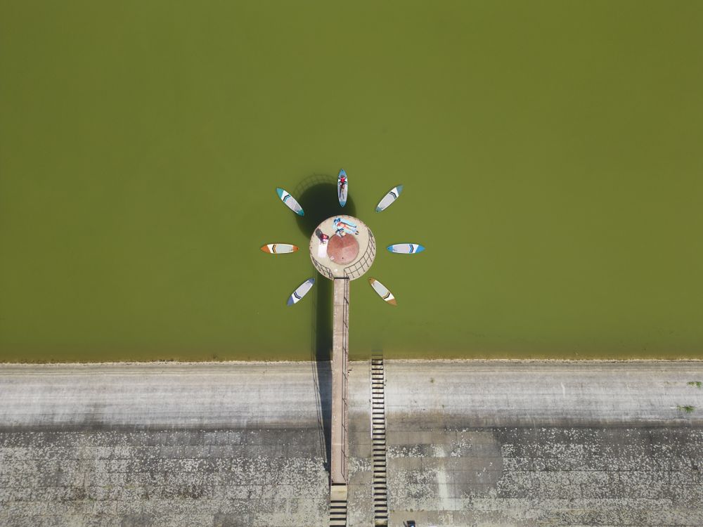 Aerial view of a multiple surfboards forming a flower around a concrete object on the lake with two women resting in the sun