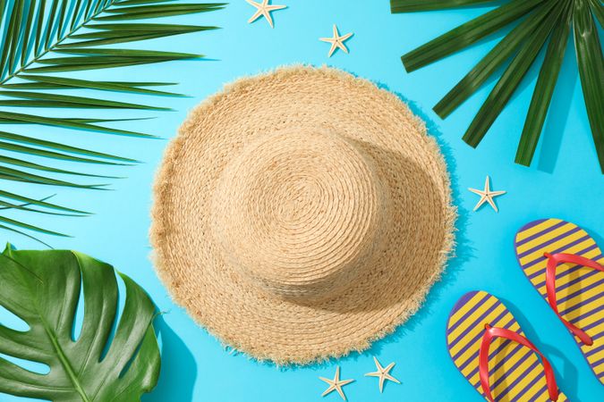 Palm leaves, flip flops, hat and starfishes on blue background, top view