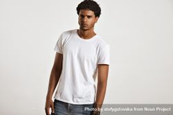 Man in blank t-shirt and jeans leaning slightly with serious expression in studio shoot bGzVB4