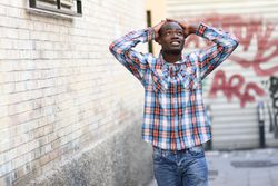 Male in plaid shirt and jeans walking down alley way with hands on his head