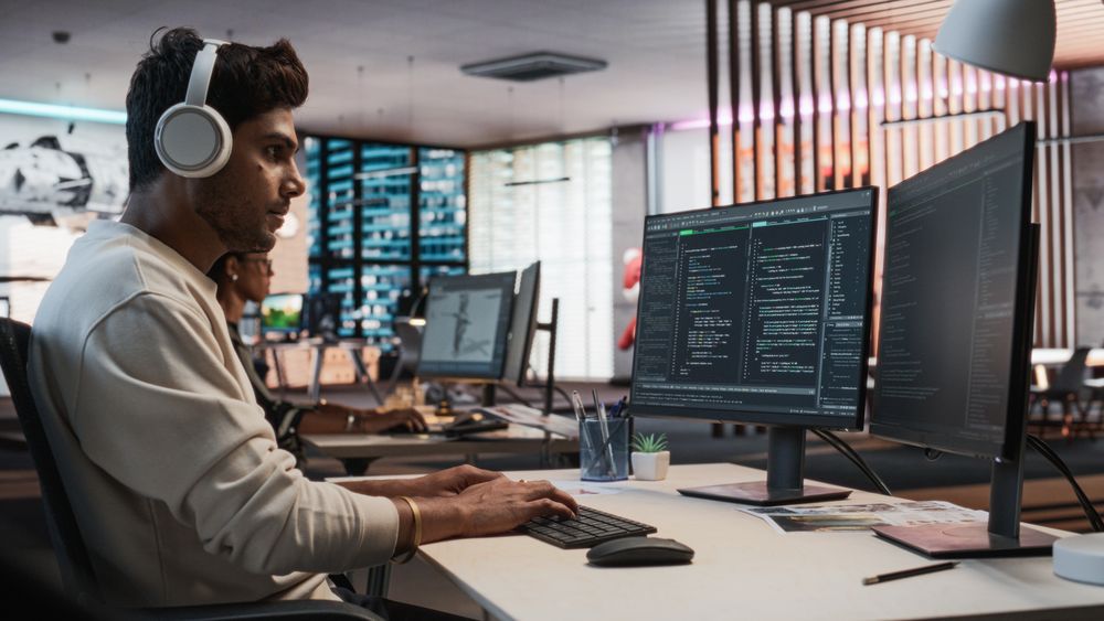 Male Indian Game Programmer Coding On Desktop Computer In Game Design Studio Diverse Office.