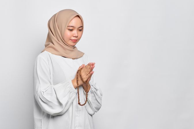 Religious Muslim woman in headscarf and light blouse with hands together in prayer
