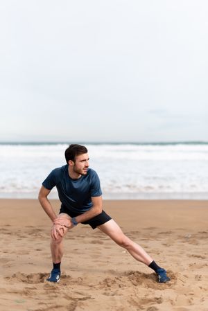 Male athlete in active wear doing exercises on legs at empty beach