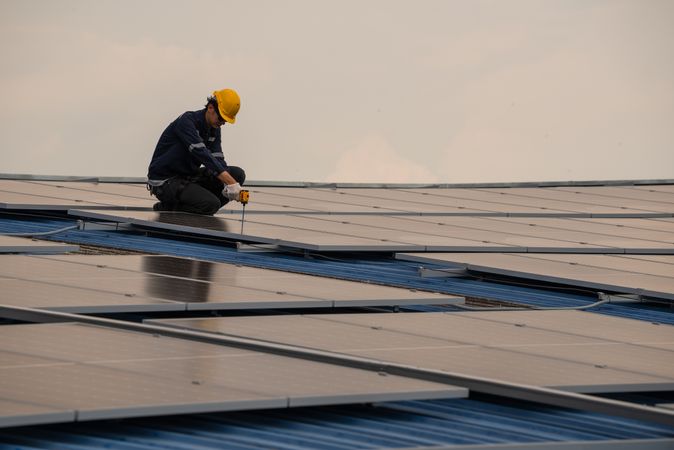 Engineer worker using electric drill repairing on solar cell panel on the roof of the factory. After service and security for industrial renewable energy concept