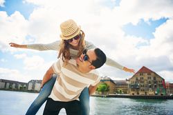 Happy couple having fun by the waterfront with man giving girlfriend piggy back