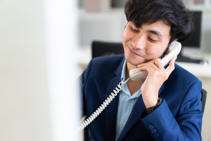 Calm Asian male in suit on satisfying phone call at work