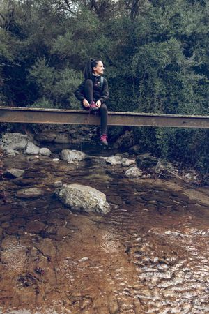 Traveler sitting on bridge above brook in woods