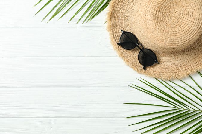 Straw hat, sunglasses and palm leaves on wooden background, space for text and top view. Summer vacation backdrop