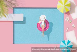 Barbie-like doll in donut ring in pool, with poolside parasols and towels 5rkql4