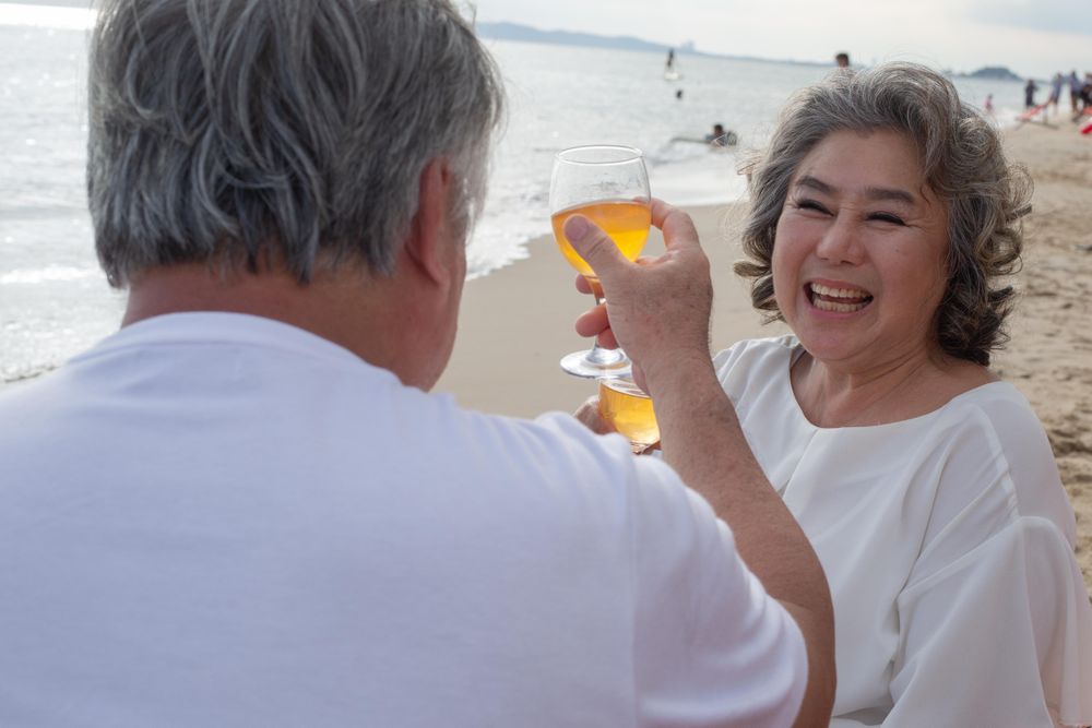 Older Asian couple relaxing on the beach and toasting with wine