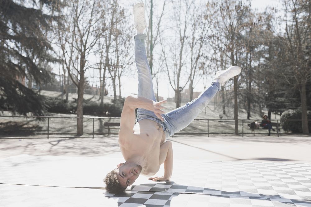 Shirtless man dancing break dance in park