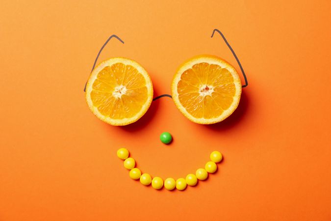 Happy face made of candies and oranges on orange background