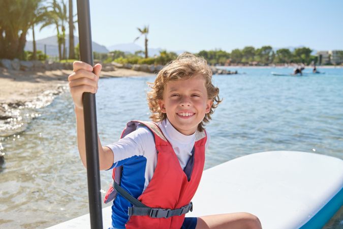 Boy with paddle sitting on SUP board on seashore