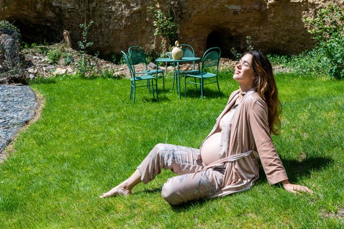 Calm pregnant woman enjoying the sun while sitting on the grass