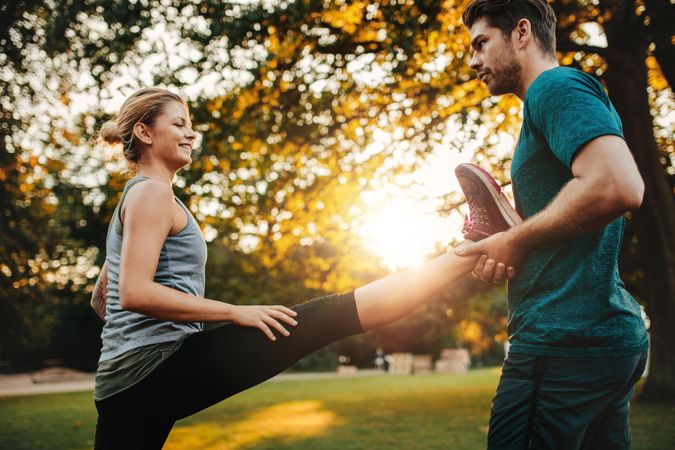 Personal trainer holding leg of woman stretching in park