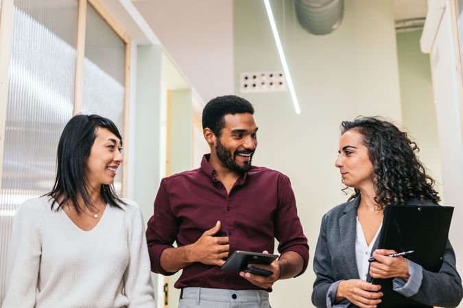 Multiracial coworkers talking happily in office corridor